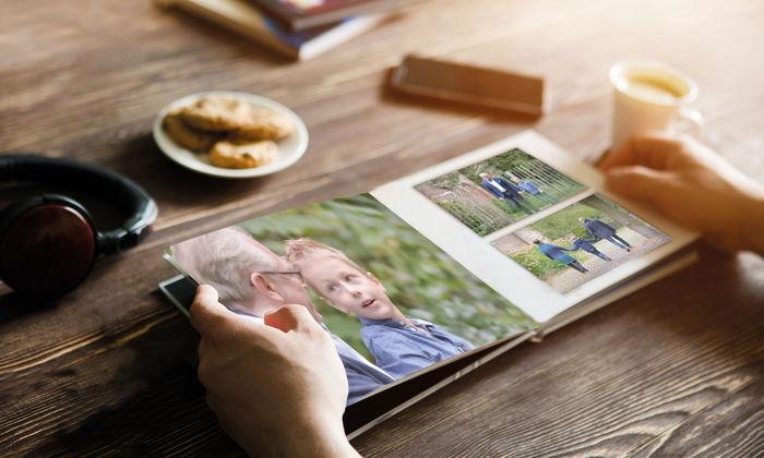 Nahaufnahme von Händen, die ein Fotobuch mit Bildern von Kindern und Familienmomenten auf einem Tisch durchblättern.